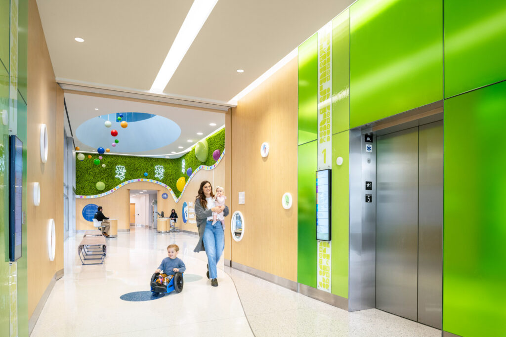 Elevator lobby walls made of colorful Bendheim glass with a child and mother approaching the elevator.