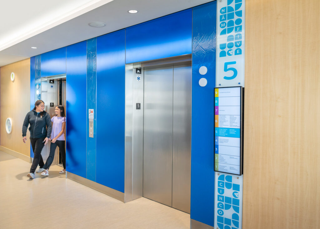 Elevator lobby walls made of colorful Bendheim glass with a child and mother leaving the elevator.