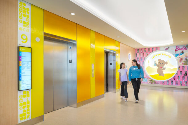 Elevator lobby walls made of colorful Bendheim glass with a child and mother leaving the elevator.